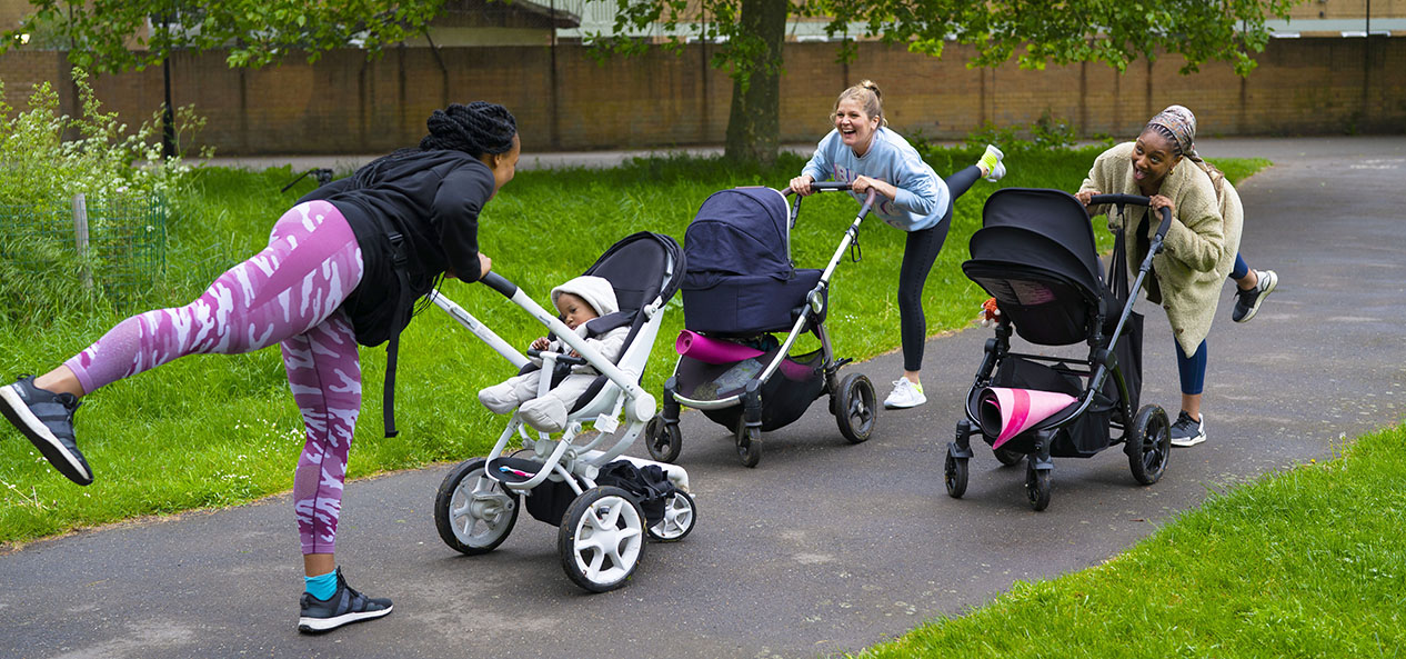 Three women stretch while pushing buggies in a park
