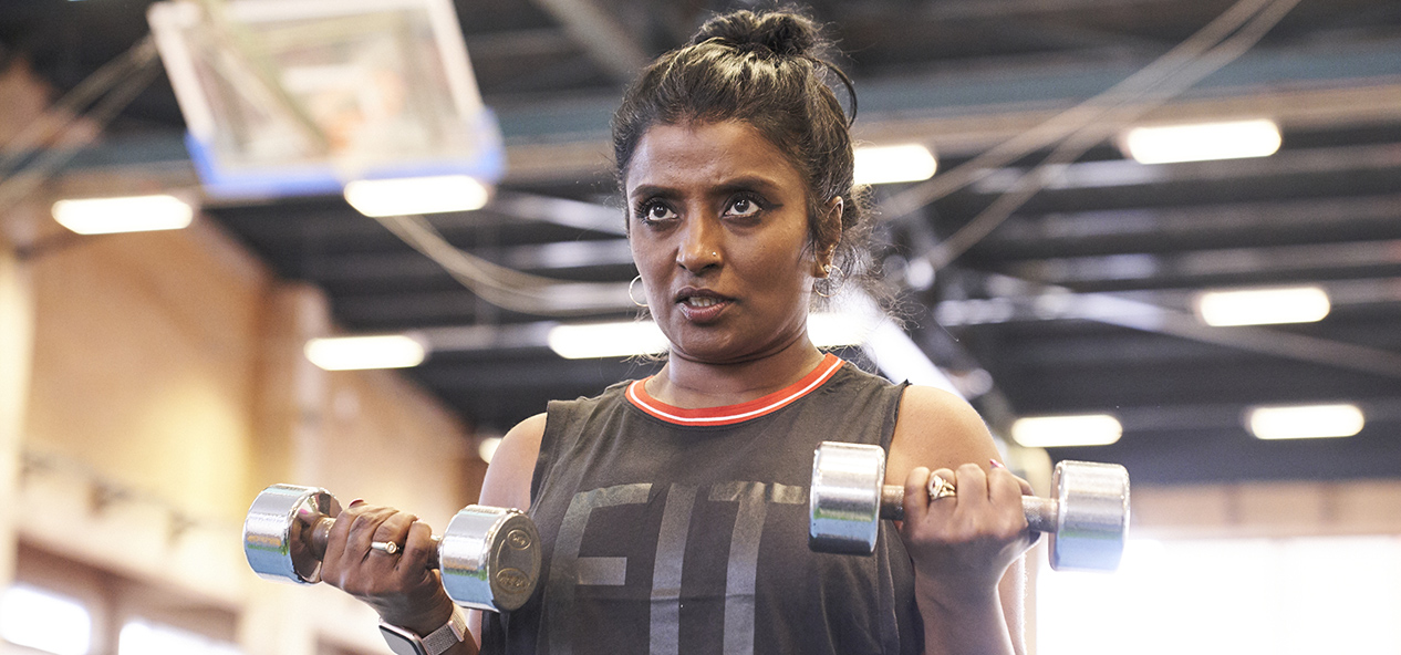 A woman does bicep curls with dumbbells in a gym