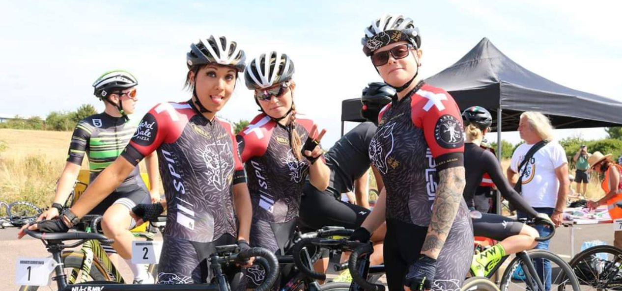 Caz and their team mate outside facing the camera in their cycling gear. 
