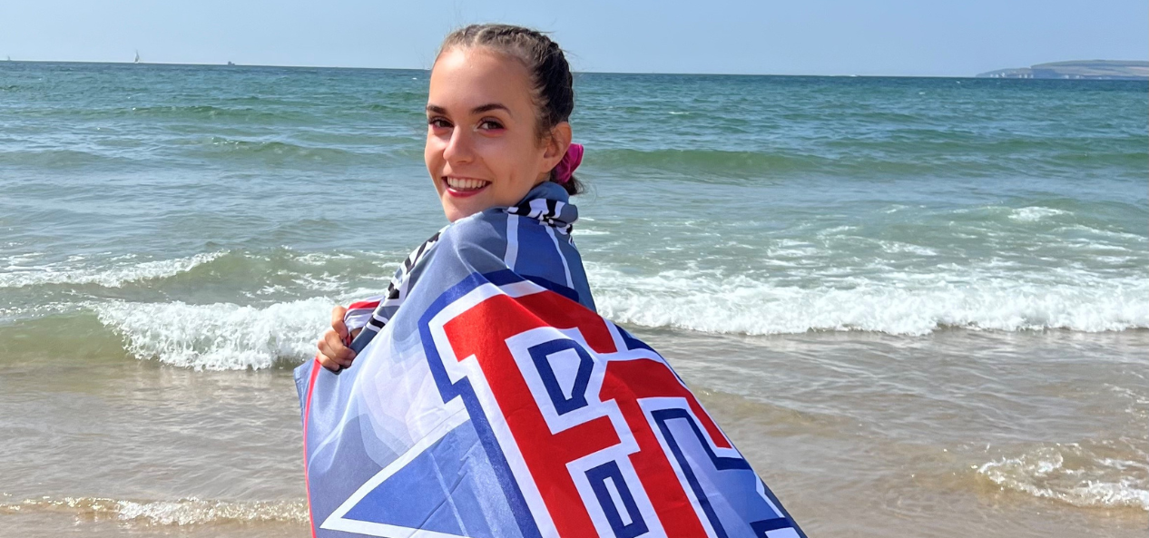 Elena, smiling on the beach with her cheer flag wrapped around her.