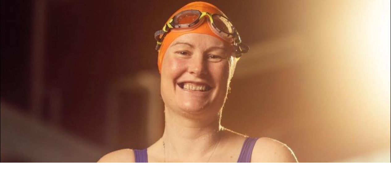 Gill wearing an orange swimming cap and smiling. 