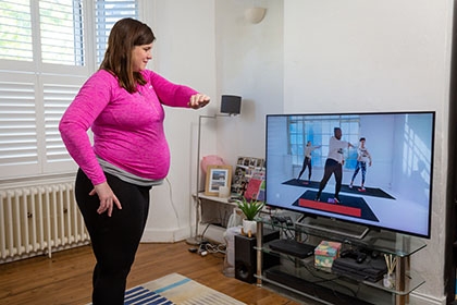 A pregnant woman exercises by copying a video session on her living room  