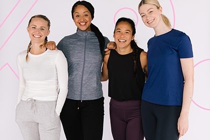 A group of girls, all of different heights, stand together while looking at the camera and smiling