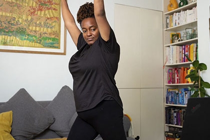 A pregnant woman keeps her arms up while copying the exercise routine from her computer in her living room