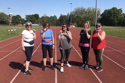 Five women pose for a photo on an athletics track