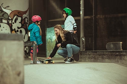 A coach teaches two young girls how to skateboard