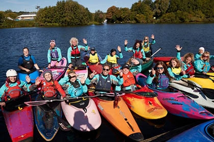 A group of women in kayaks and on paddle boards float next to each other and pose for a photo.