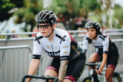 Caz cycling in her black and white cycling gear on their bike outside down a road with their team mate behind them. 