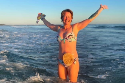  wearing her bikini, smiling with her arms raised in the air, whilst standing in the sea. 