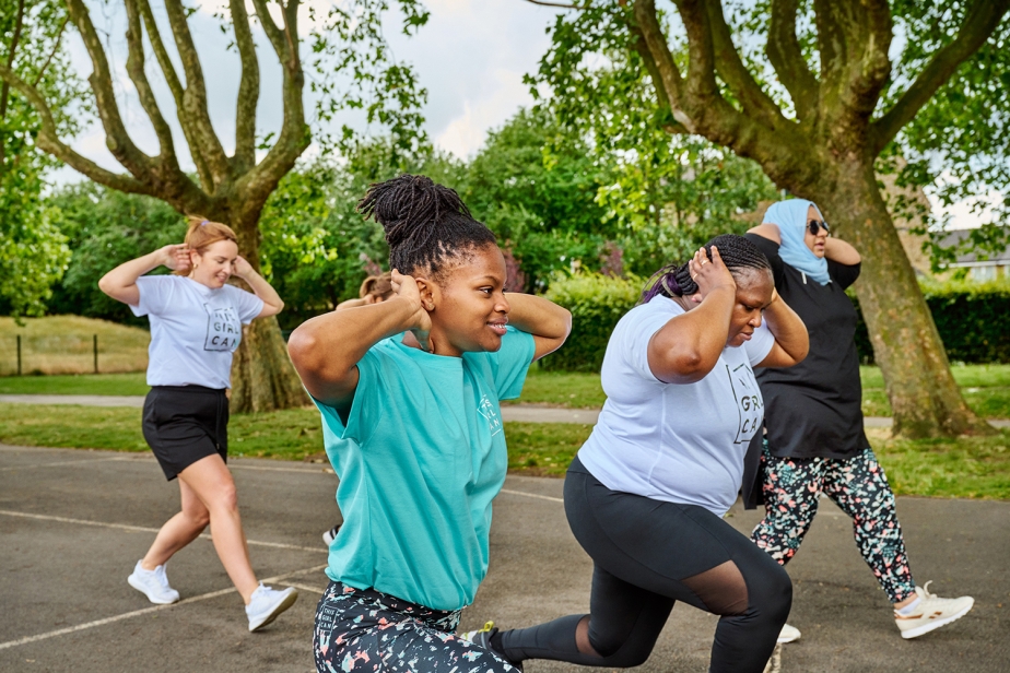 A group of women, wearing This Girl can activewear, perform walking lunges in a park