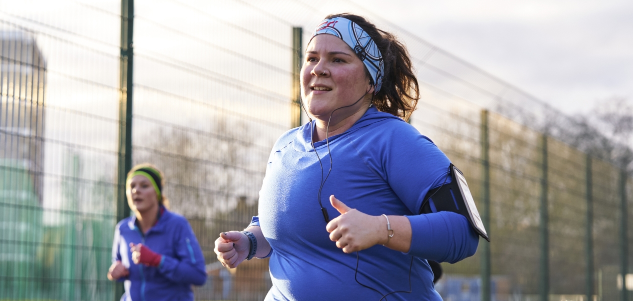 A woman runs in a park, with another woman running in the background