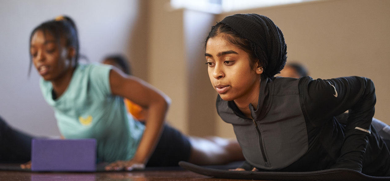 Two women perform a yoga pose while laying face down on the ground