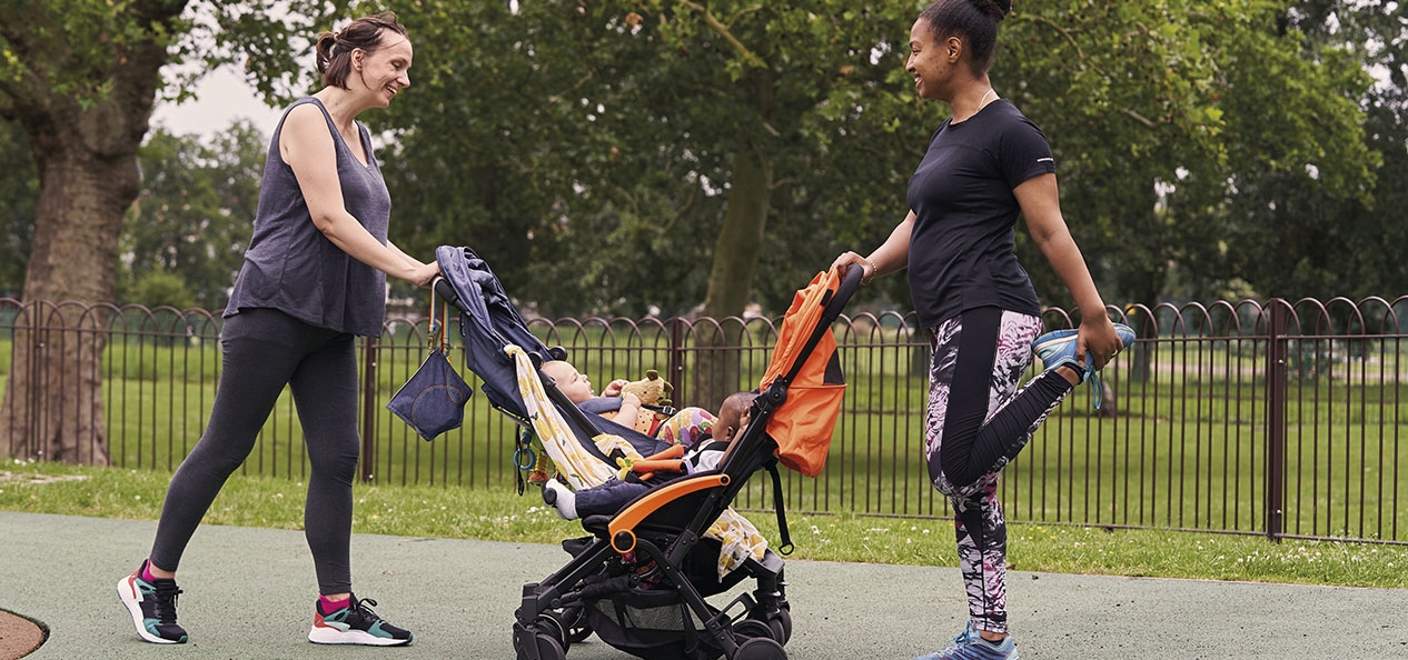 Two women stretch in a park, while leaning on push chairs