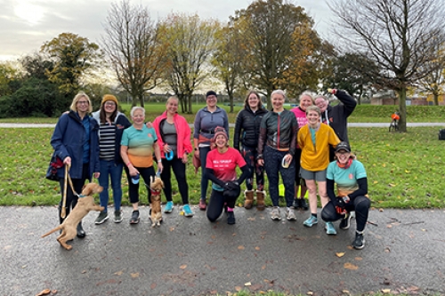 A group of women in exercise clothes pose in a park for a photo