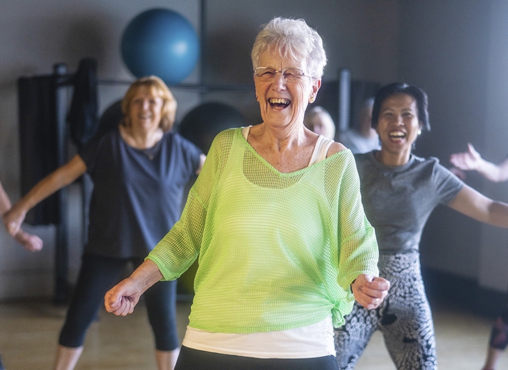 An older woman smiles at the front of an exercise class