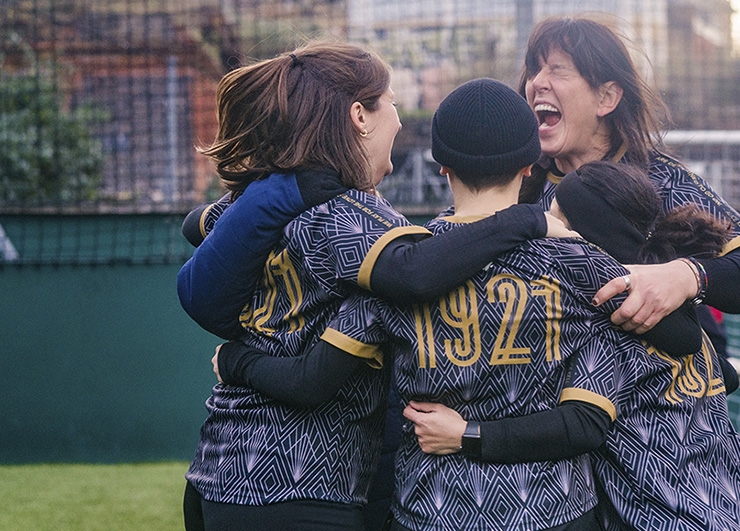 A group of women footballers huddle together to celebrate