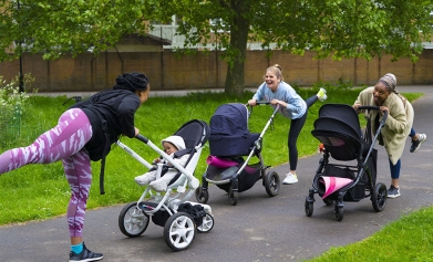 Three women stretch in a park, leaning on their buggies